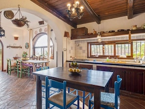 A rustic kitchen with a wooden table and chairs, a window with a view, and a hanging light fixture. - Villa in Partinico Near the Beach (Partinico)