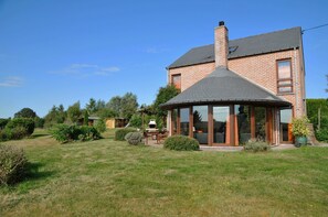 Een tweelaags bakstenen huis met een grote glazen conservatorium, een schoorsteen en een verzorgd gazon.