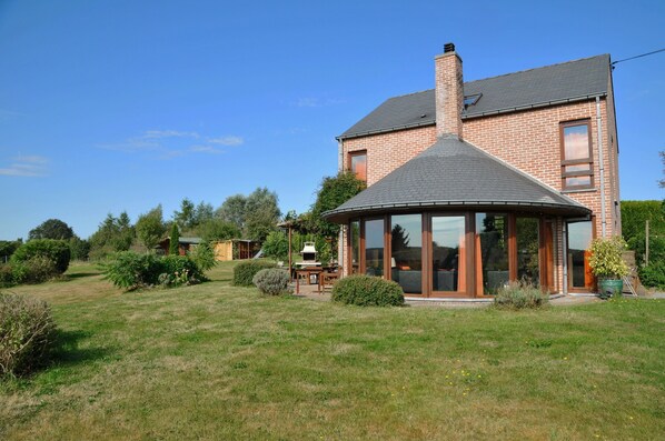 A two-story brick house with a large glass conservatory, a chimney, and a well-maintained lawn.