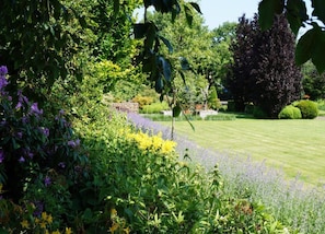 A lush garden with a variety of plants and flowers, a well-maintained lawn, and a stone wall in the background. - Chalet in Oignies With Wooded Surroundings (Viroinval)