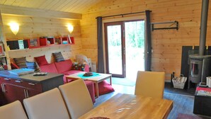 Interior acolhedor de uma cabana com uma mesa de jantar de madeira, cadeiras, um sofá vermelho, uma área de cozinha com fogão e uma janela grande.