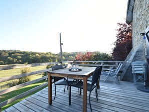 A wooden deck with a table and chairs, overlooking a grassy field and trees. - Quaint Holiday Home in Beauraing Belgium With Private Garden (Beauraing)