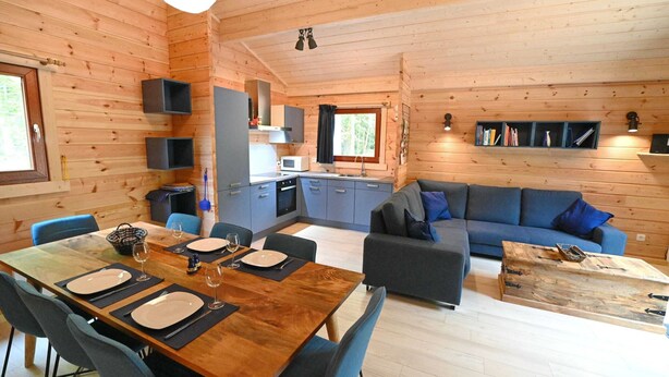A wooden cabin interior with a dining area, kitchen, and living room.