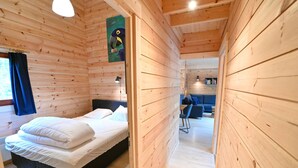 A wooden cabin interior with a bed, a desk, and a sofa.
