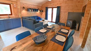 A wooden cabin interior with a dining area, sofa, kitchen, and a fireplace.