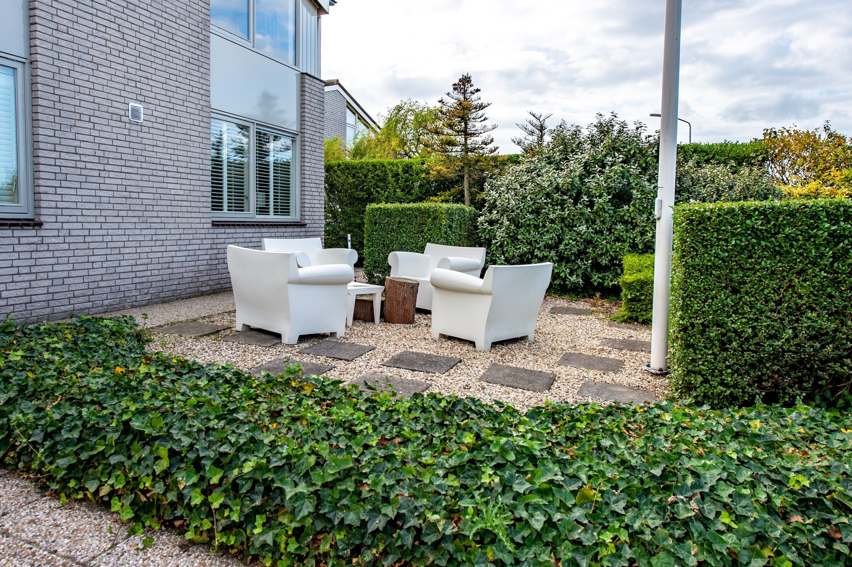 A patio with white outdoor furniture, a stone pathway, and a hedge.