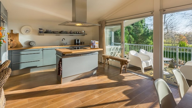 A modern kitchen with a large island, wooden flooring, and a view of a balcony with outdoor furniture. - Bungalow Near Marina and Beach Kamperland (Kamperland)