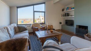 A living room with a large window, a sofa, a chair, a coffee table, and a TV. - Bungalow Near Marina and Beach Kamperland (Kamperland)