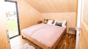Ein Schlafzimmer mit Holzwänden, einem großen Bett, einem kleinen Tisch und Blick ins Freie.