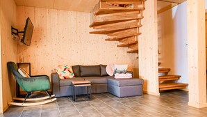 Ein modernes Wohnzimmer mit Holzboden, einem grauen Sofa, einem Schaukelstuhl und einem kleinen Tisch.