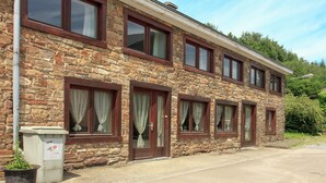 A two-story stone building with multiple windows and a visible trash bin. - Holiday Home in Ardennes With Sauna & Nature (Manhay)