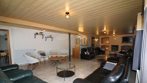 A spacious living room with a green leather sofa, a black leather sofa, and a glass coffee table. There are several chairs and a fireplace in the background. - Holiday Home in Ardennes With Sauna & Nature (Manhay)
