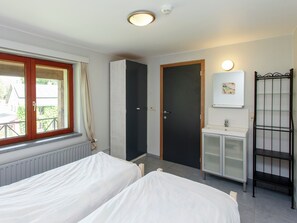 Une chambre avec deux lits, une armoire, une salle de bain avec un miroir et une fenêtre avec des rideaux.