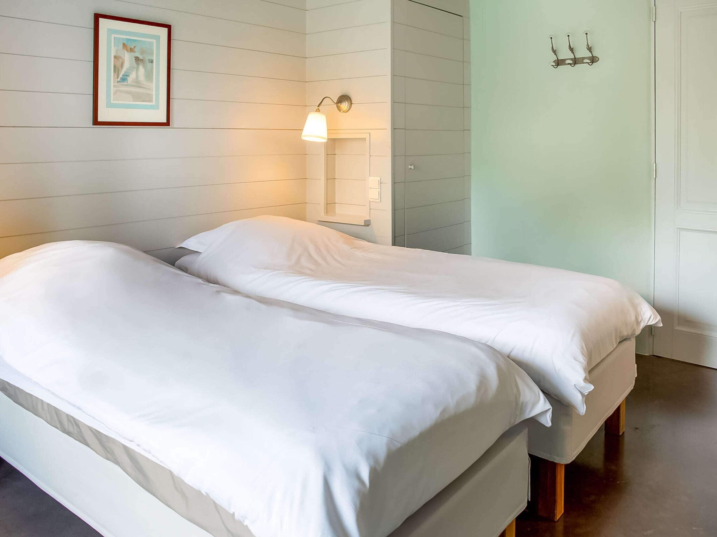 A double bed with white bedding in a room with white walls and a light green accent wall.