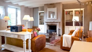 A living room with a fireplace, bookshelves, a desk with a lamp, and leather furniture. - Getaway With Sauna in Falaen (Onhaye)