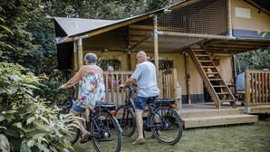 A wooden deck with bicycles, a covered area, and a staircase leading to a building. - Chalet in Baalse Hei With Modern Comforts (Turnhout)