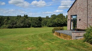 Un bâtiment moderne en briques, doté d’une grande porte vitrée, d’une vaste pelouse et bordé d’une forêt.