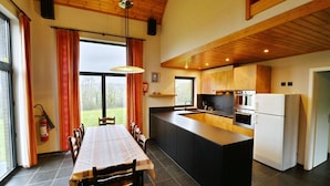 Une cuisine moderne dotée d’un îlot central, d’un plafond en bois et de grandes fenêtres.