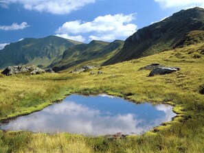 Paisaje montañoso con un pequeño estanque y terreno cubierto de hierba.