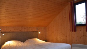 Een kamer met houten lambrisering, een bed, twee bedlampen en een raam met gordijnen.