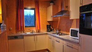 Een compacte keuken met houten kastjes, een roestvrijstalen spoelbak, een fornuis en een magnetron.
