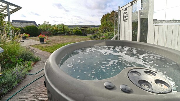 Un bain à remous dans un jardin, avec une terrasse en bois, entouré de plantes en pot et d’un potager.