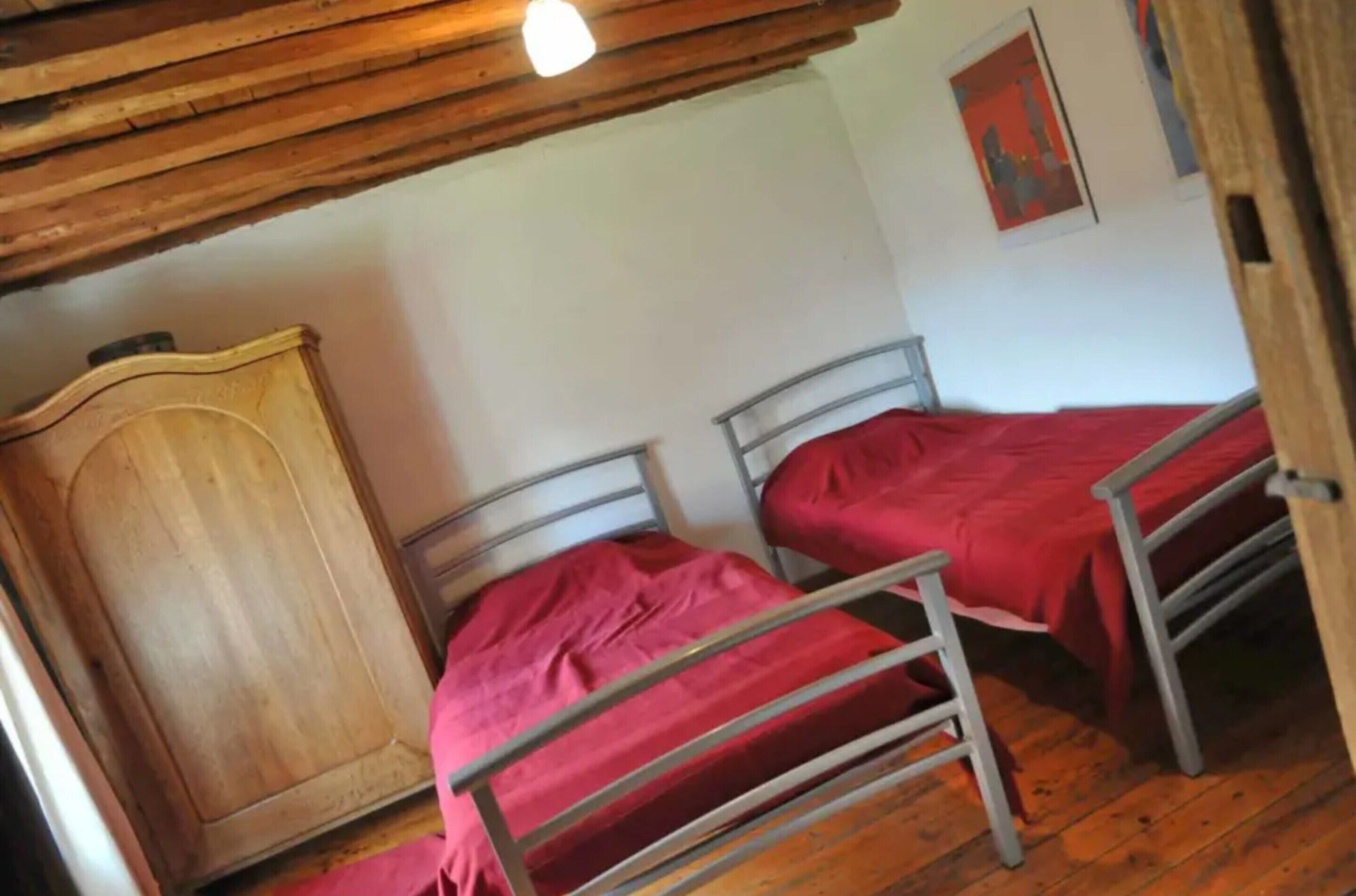 A room with two metal beds, a wooden wardrobe, and a wooden ceiling.