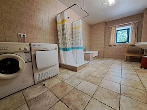 A bathroom with a washing machine, a bathtub, and a window with curtains. - Gîte L'olivier à Filly - Nadrin, Entre Houffalize et La Roche-en-ardenne (Houffalize)