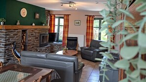 A cozy living room with a fireplace, a stone wall, a television, and a dining area with a table and chairs. - Gîte L'olivier à Filly - Nadrin, Entre Houffalize et La Roche-en-ardenne (Houffalize)