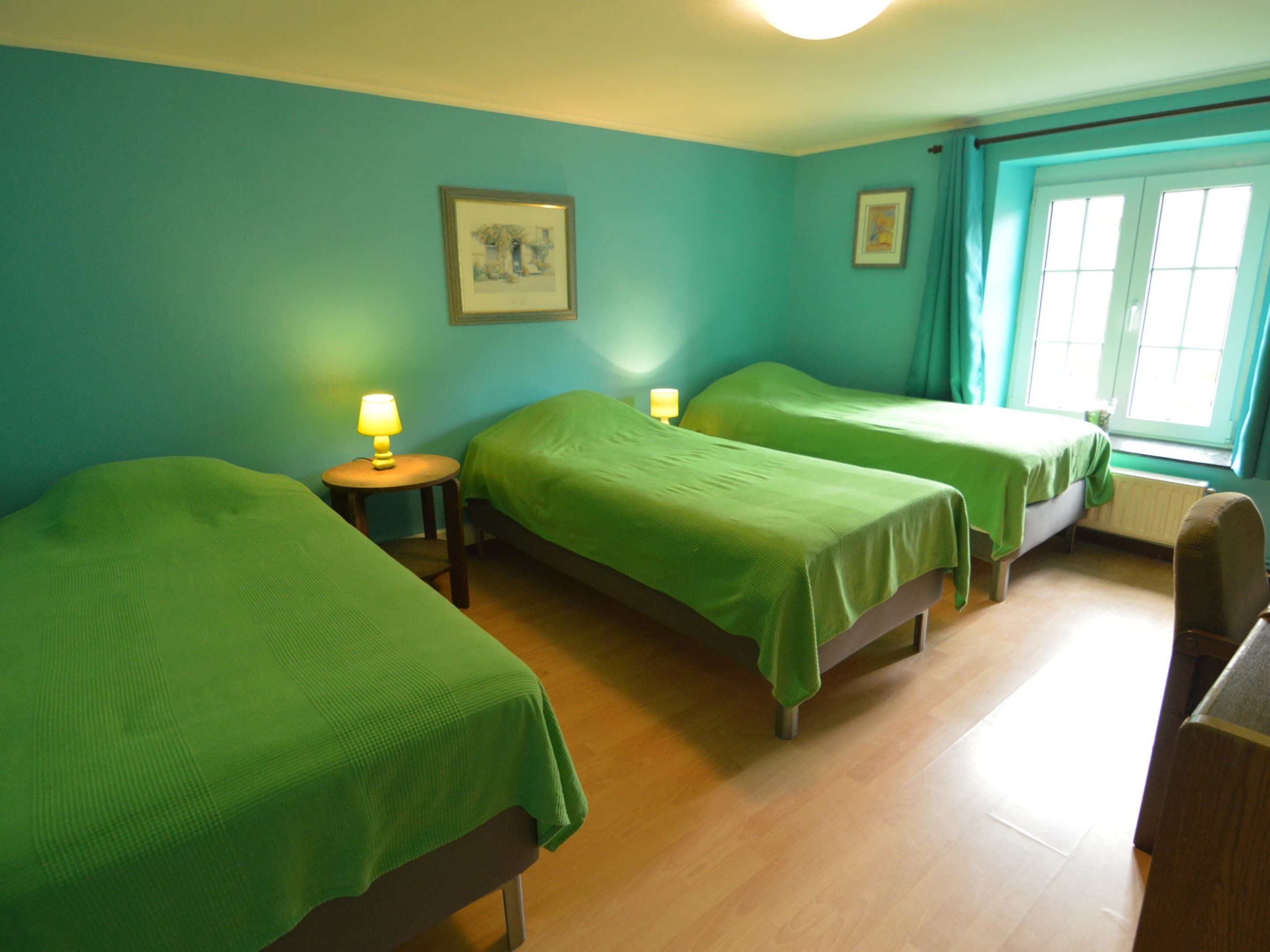 A room with three beds, two lamps, and a window with curtains.