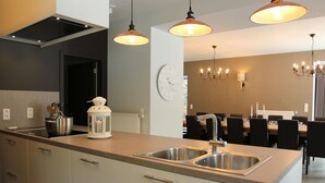 A modern kitchen with a central island, stainless steel sinks, pendant lighting, and a dining area with a chandelier.