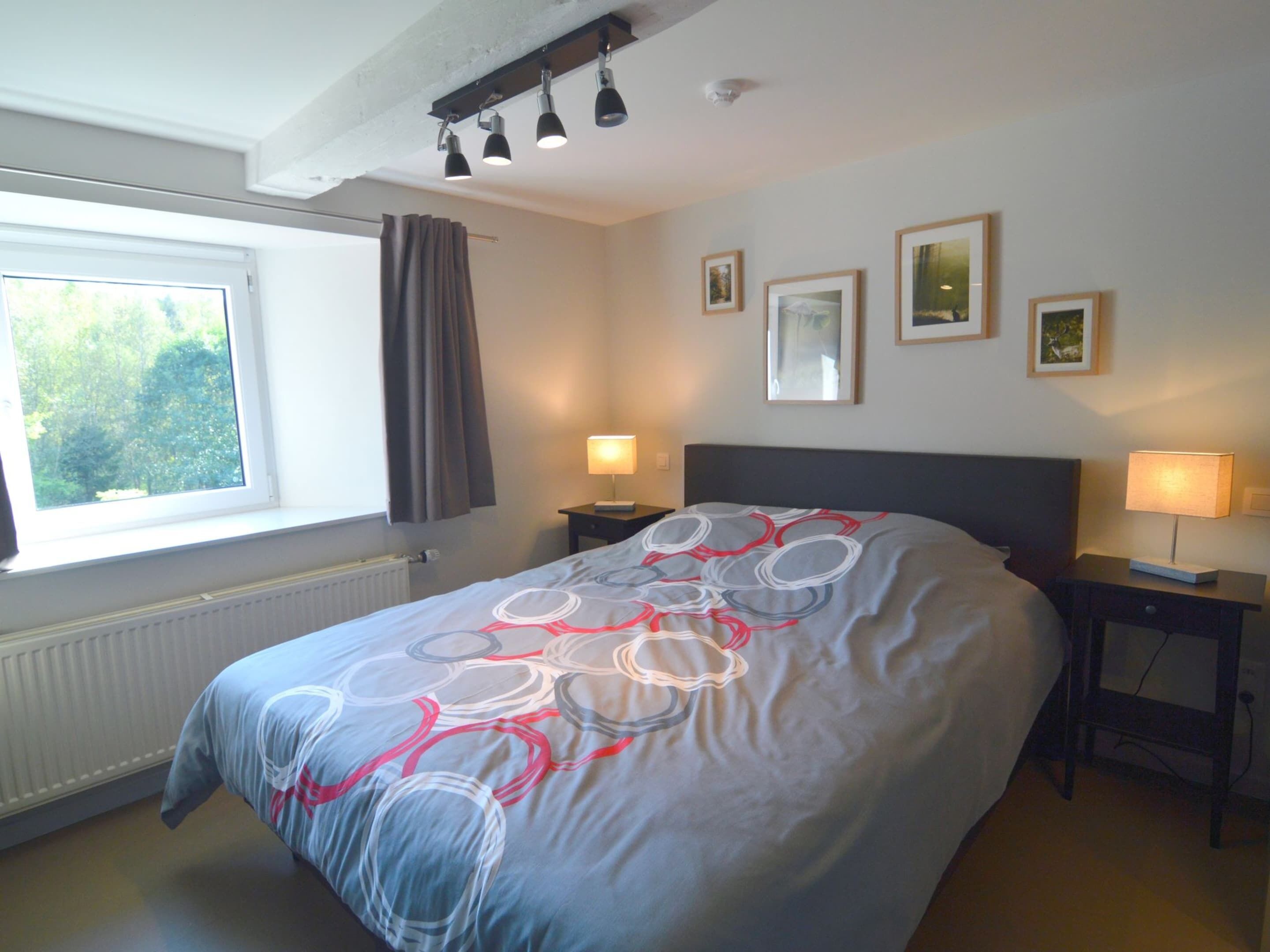 Une chambre à coucher comprenant un lit, deux tables de chevet, une fenêtre avec des rideaux et des lampes fixées au mur.
