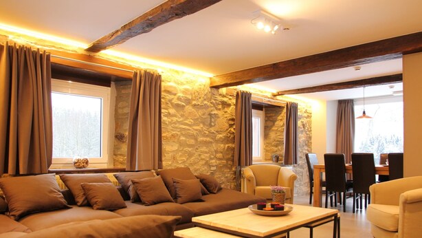 A cozy living room with a stone wall, a sofa, a coffee table, and a dining area with chairs and a table.