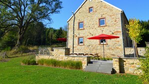 A stone building with a sloped roof, a small porch with steps, and two red umbrellas.
