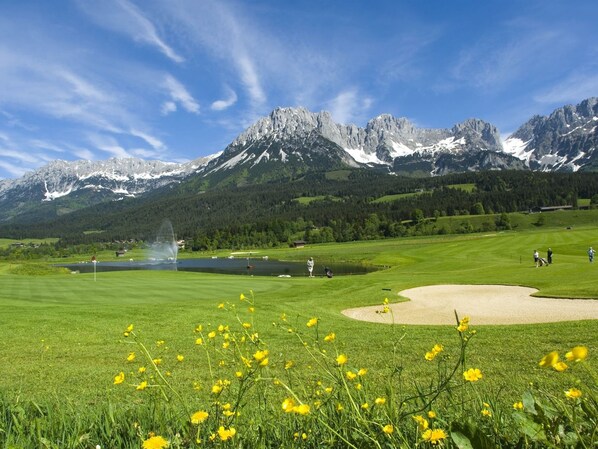 Um campo de golfe com um lago, montanhas e um céu limpo.