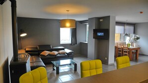 A modern living room with a sofa, a coffee table, and yellow chairs. There is a television mounted on the wall and a fireplace.