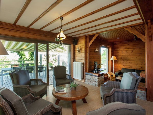 A wooden interior with a round table, wicker furniture, and a stone fireplace.