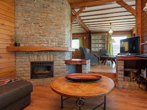 A rustic interior with a stone fireplace, wooden beams, a television, and a dining area.