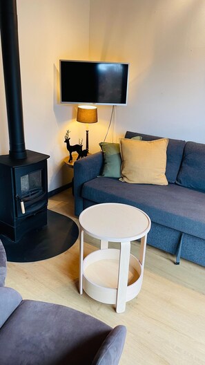 A living room with a sofa, a round table, a TV, a lamp, and a wood-burning stove.