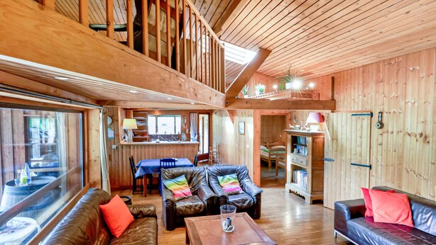 Uma cabana de madeira espaçosa com quarto no mezanino, sala de jantar e sala de estar com sofás de couro e mesa de centro.