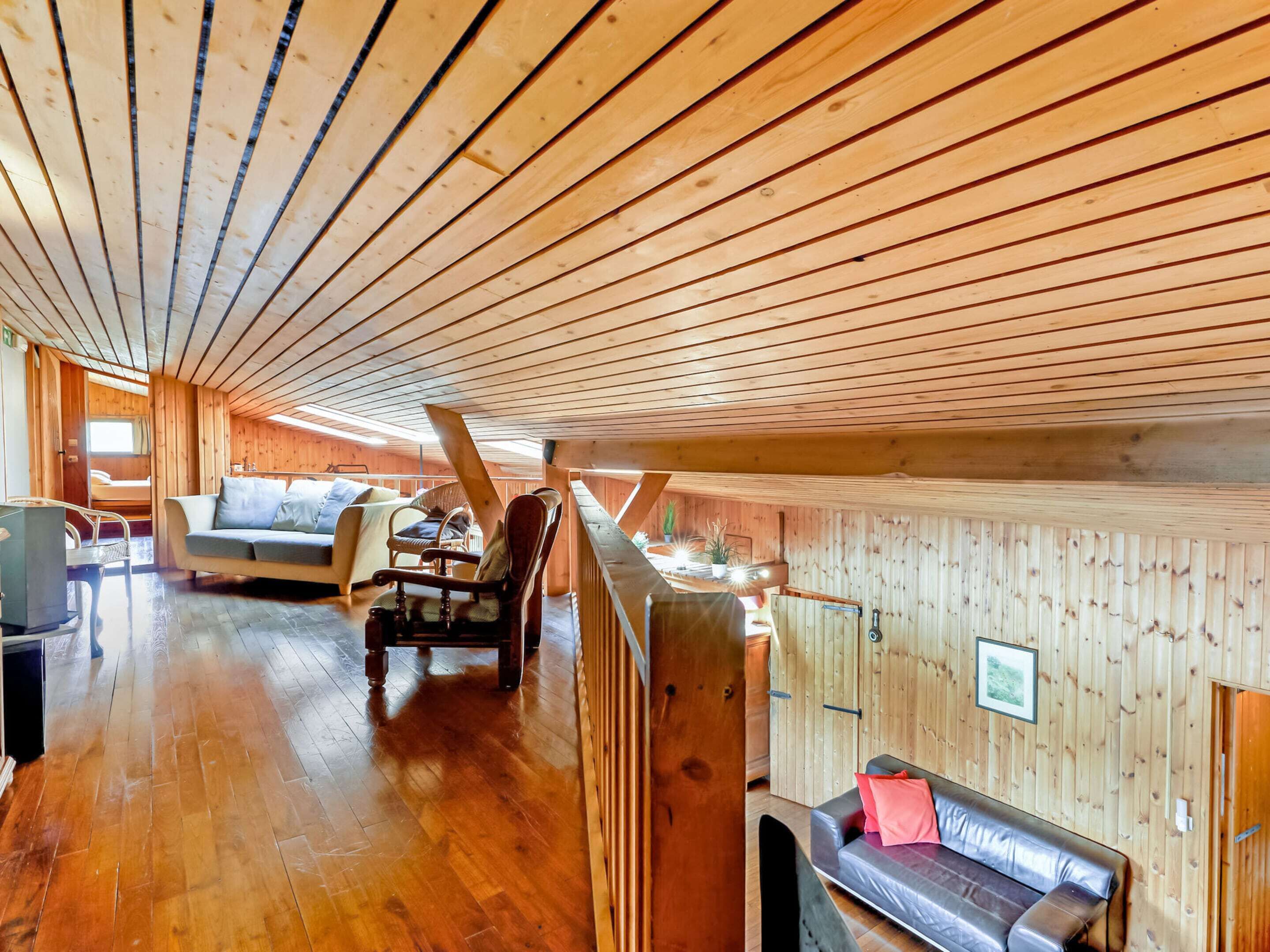 A spacious loft with wooden walls and a high ceiling. There are two seating areas with sofas and chairs.