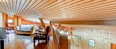 A spacious loft with wooden walls and a high ceiling. There are two seating areas with sofas and chairs.