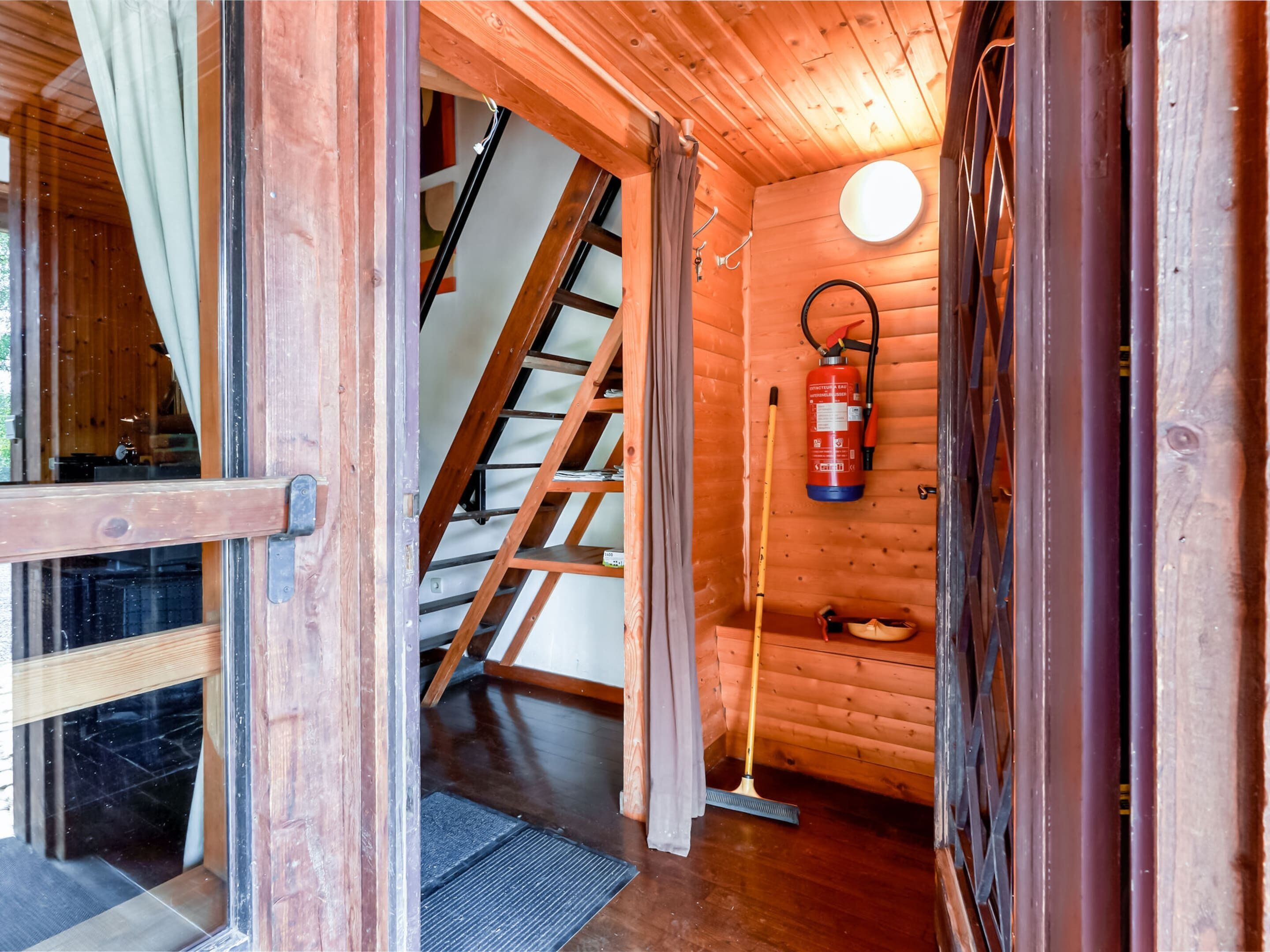 A wooden interior with a staircase, a fire extinguisher, and a door.