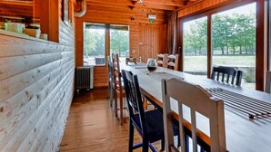 Uma cabana de madeira com área de jantar, que inclui uma mesa comprida e cadeiras, janelas amplas e vista para o exterior.