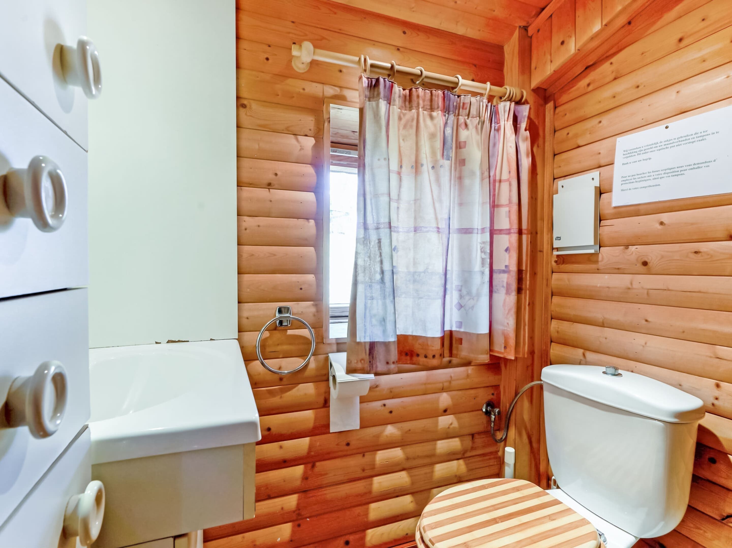 A wooden cabin bathroom with a toilet, sink, and a shower curtain.