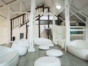 A spacious interior with white, modern seating arrangements and a high ceiling with exposed wooden beams. - Mountain Retreat for Group (Daverdisse)