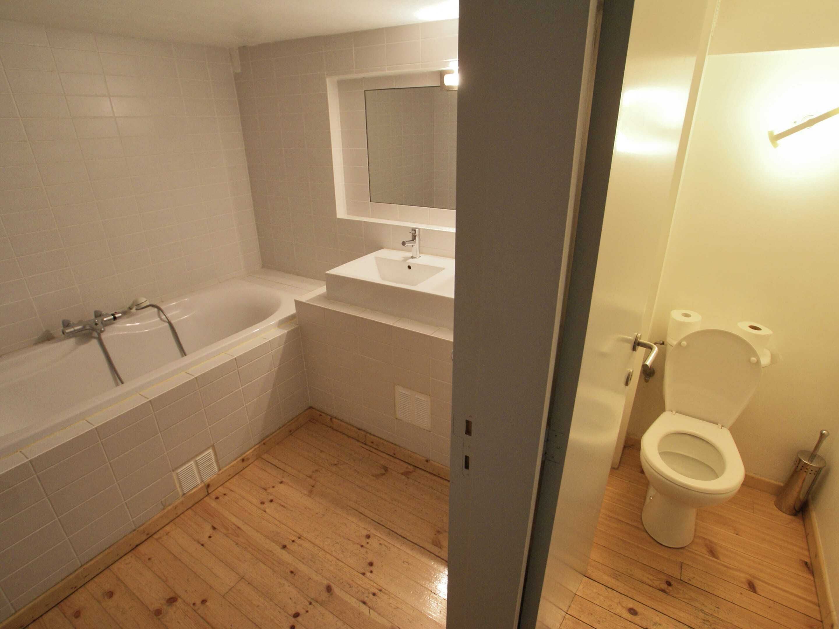 A bathroom with a bathtub, sink, mirror, toilet, and wooden flooring.