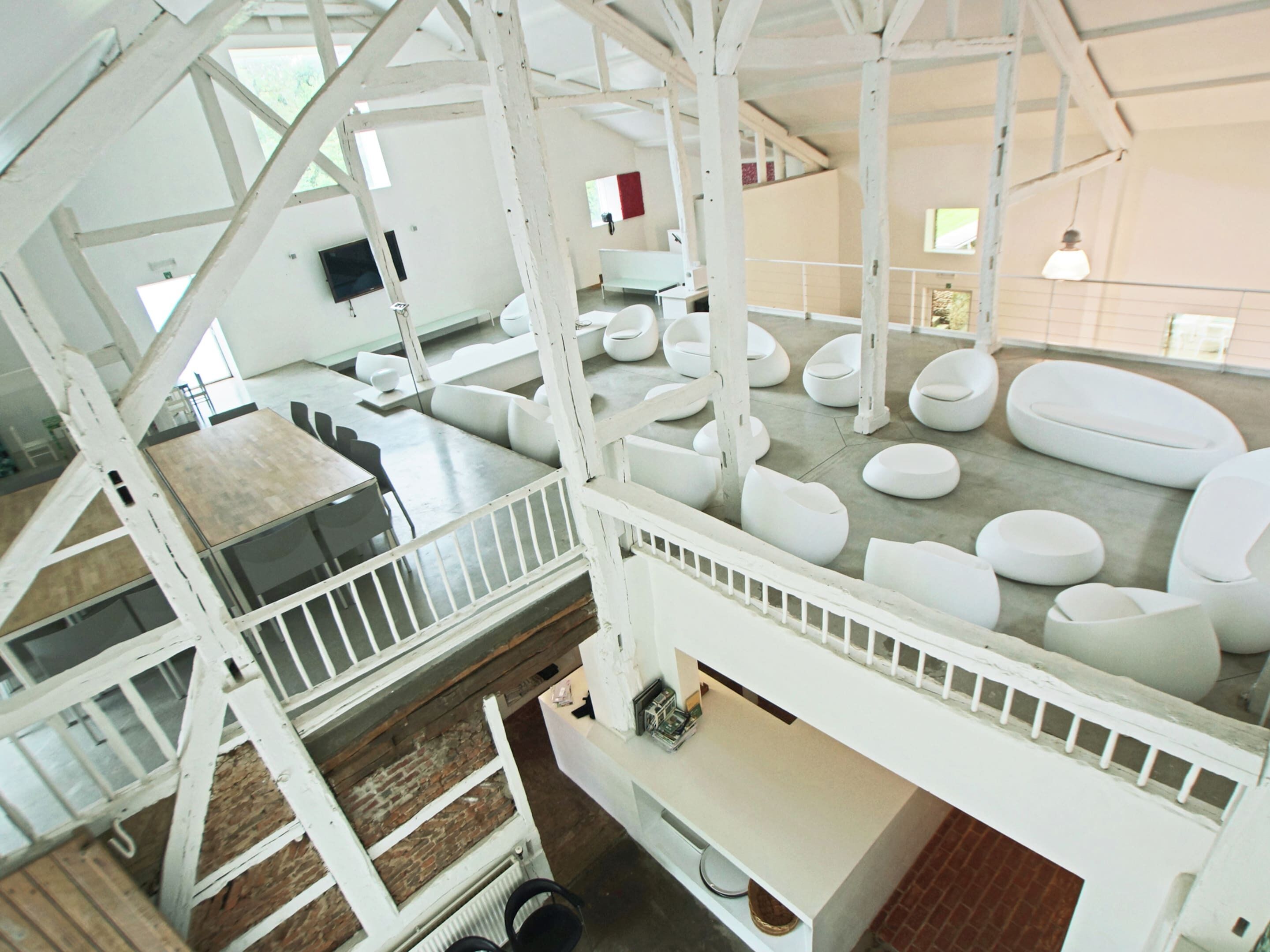 A modern interior with a high ceiling, white structural beams, and a variety of seating arrangements.