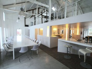 Une salle de conférence moderne, dotée d’une longue table et de chaises, d’un coin cuisine et d’un bar avec des tabourets.