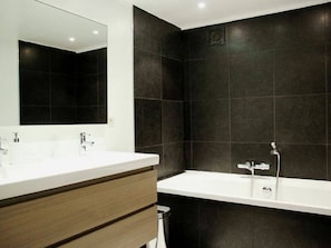 Ein modernes Badezimmer mit einem weißen Waschbecken, einem Spiegel und einer Badewanne.